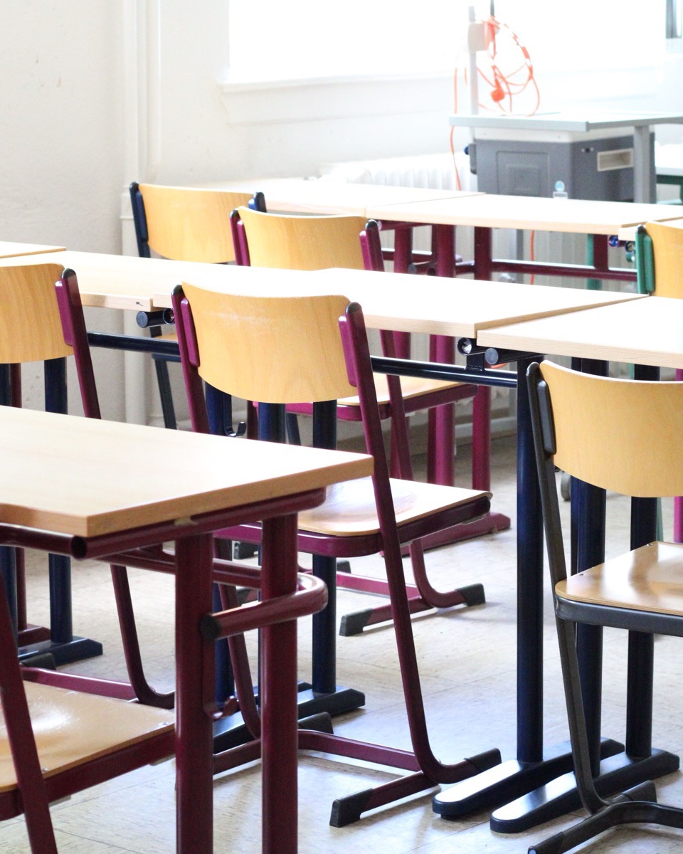 Rows of empty desks and chairs in a sunlit classroom